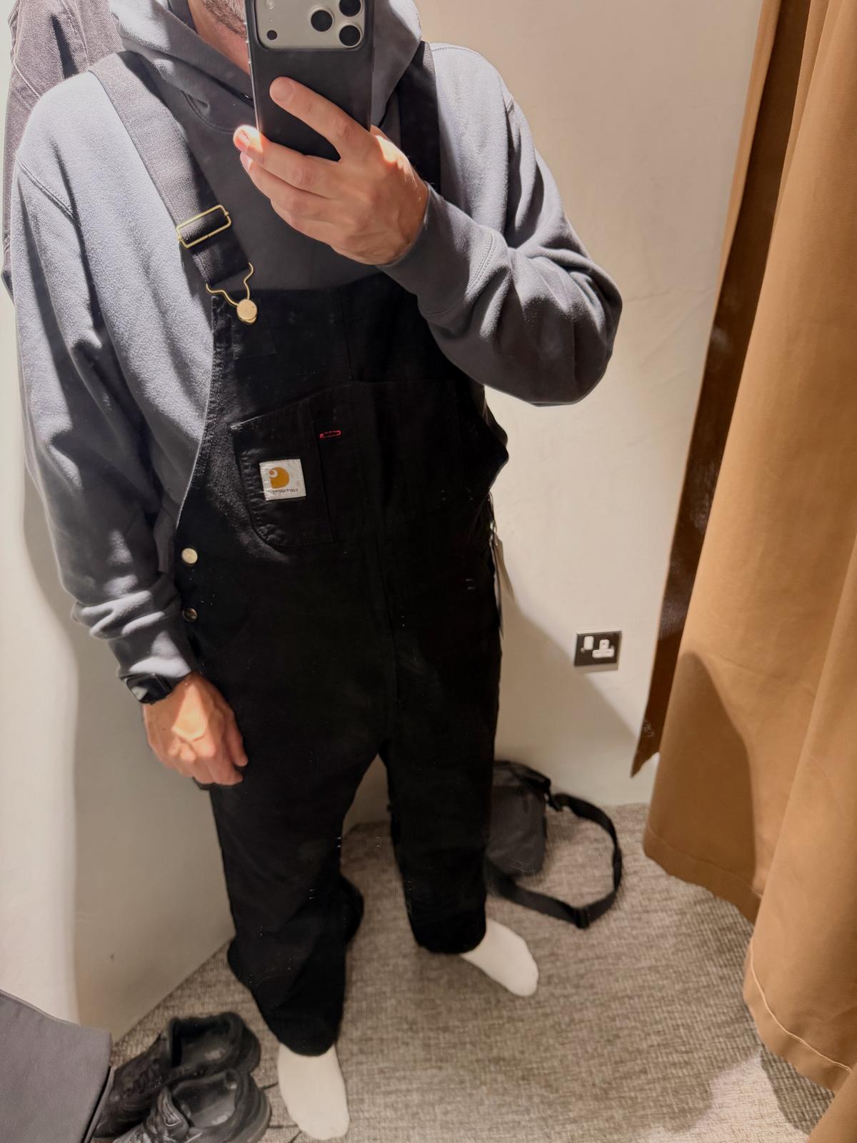 Mirror selfie of me trying on black Carhartt WIP dungarees