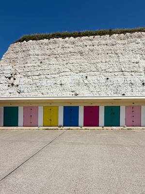 Beach huts with coloured doors below a white chalk cliff
