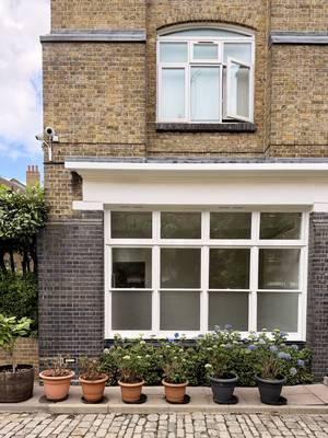 A brick building with a large window with cobblestones and potted plants outside.